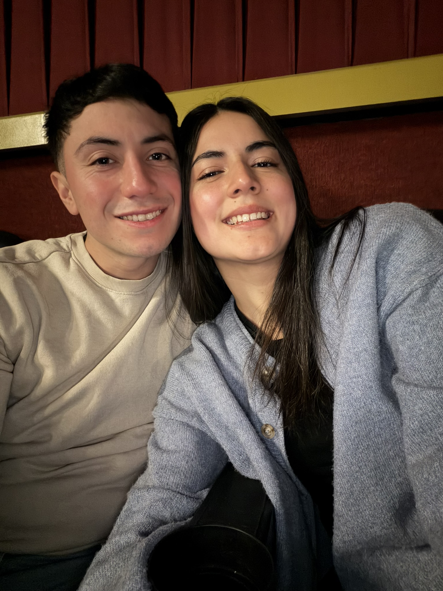Selfie cercana de Javier y Sabrina sonriendo ante un fondo rojo.